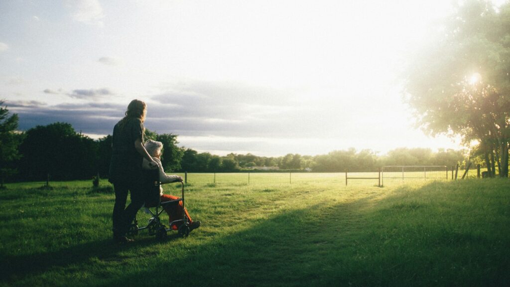 Mantelzorger wandelt met oudere in rolstoel in de natuur tijdens mantelzorg dagelijks leven