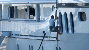 Persoon reinigt romp van jacht met touwen tijdens onderhoud volgens boot schoonmaak tips